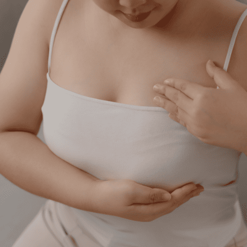 Mulher examinando a mama com a mão, representando o autoexame e a atenção a possíveis nódulos mamários.